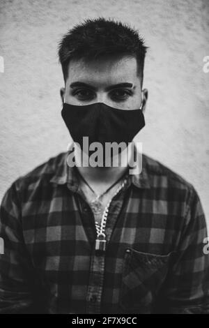 Vertical grayscale shot of a young Spanish man wearing a face mask Stock Photo