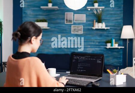 Back view of student developer writing javascript using analytic program while sitting at desk table in living room. Freelancer software developer programer programming digital code Stock Photo