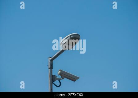 CCTV security camera on street lamp post closeup on blue sky background Stock Photo