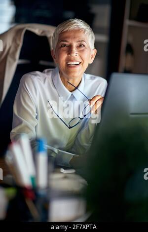 A senior business woman is posing for a photo at the desk in a pleasant atmosphere at the workplace. Business, office, job Stock Photo