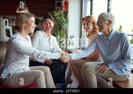 Group of senior female office staff getting know their new young female colleague while taking a break in a friendly atmosphere at workplace. Business Stock Photo