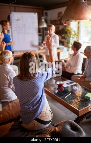 A young business woman raising a hand to ask a question her female colleague holding a presentation in a pleasant atmosphere at workplace. Business, o Stock Photo
