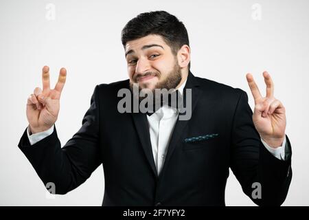 Handsome man showing with hands and two fingers air quotes gesture, bend fingers isolated on white background. Guy in black tuxedo. Not funny, irony Stock Photo