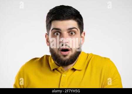 Frightened man afraid of something and looks into camera with big eyes full of horror over white wall background. Stock Photo