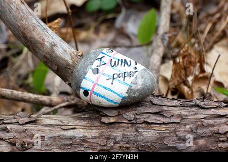 Cheeky painted rock on a log in the forest: paper beats rock! - Kindness rock that reads "I win!" on paper that sits on a log in the forest Stock Photo