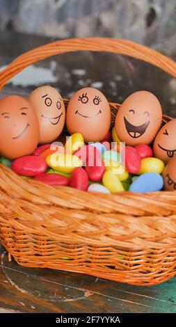 Stack of eggs with hand drawn faces on straw basket with colorful candy, easter preparation, holiday mood concepts Stock Photo