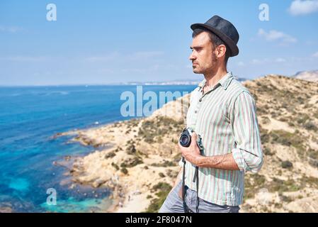 A young traveler standing in a tourist area where you can see beautiful colors of the sea and the beach Stock Photo