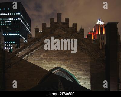 View of the top of the stone wall of a church at night with buildings in the background Stock Photo