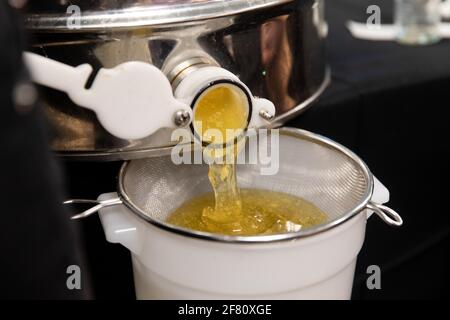 Fresh honey coming out of a container being filtered in a screen to go in another container Stock Photo