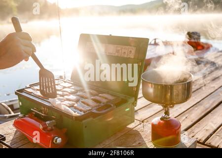 small portable green stove with bacon and a pot on a second propane stove Stock Photo