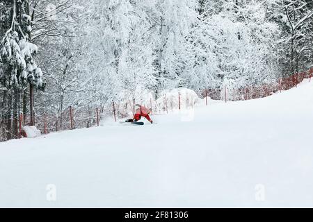 Male snowboarder in a red suit rides on the snowy hill with snowboard, Skiing and snowboarding concept.