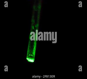 Plastic optical fiber transmitting green light against a dark background, illustrating fiber optic light transmission and optical technology Stock Photo