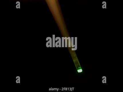 Plastic optical fiber transmitting green light against a dark background, illustrating fiber optic light transmission and optical technology Stock Photo