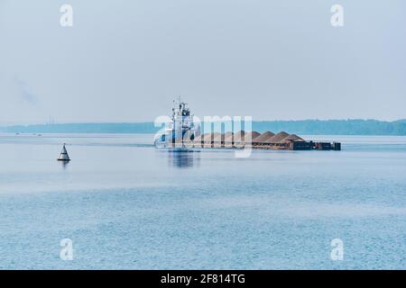 towboat pushes dry bulk cargo barge with sand on the river in the morning haze Stock Photo