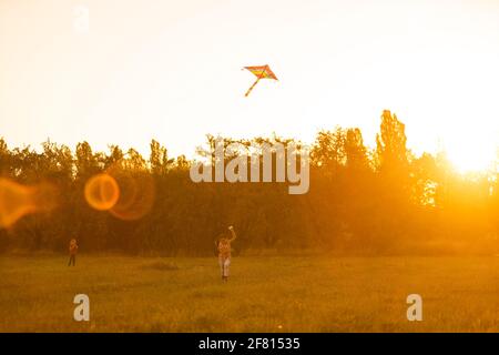 Two kids flies a kite over sunset in park Stock Photo
