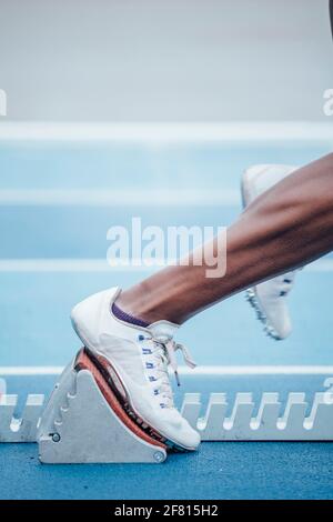Unrecognizable afro sportswoman in sportswear beginning race from crouch start position on starting blocks Stock Photo