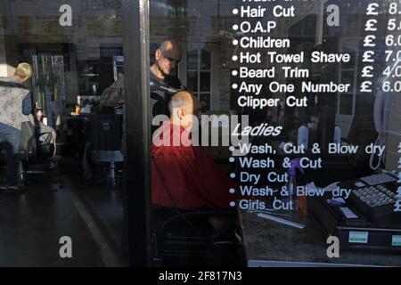 Board at barber shop with prices and barber in background drying the hair of a customer. Stock Photo