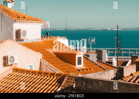 View of tiled triangle European rooftops with clay tiles, tv aerials, windows, and external on-wall units of air conditioners, with a beautiful river Stock Photo