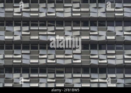 A grey facade of a modern office business high-rise building with rows of windows and plenty of small concrete blocks each one has its own random hori Stock Photo