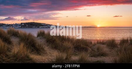 Instow, North Devon, England. Saturday 10th April 2021. UK Weather. After a day of sunshine and a strengthening breeze, the final rays of April sunshine light up the dunes overlooking the beach at the picturesque coastal village of Instow. Credit: Terry Mathews/Alamy Live News Stock Photo