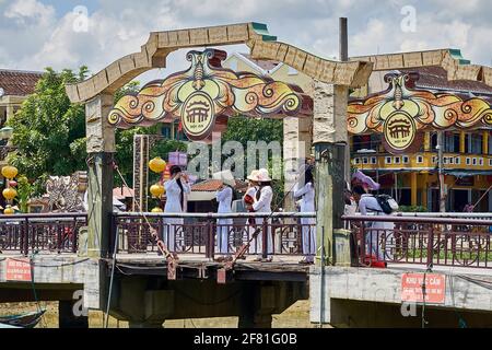 Group of Vietnamese women wearing traditional Ao Dai taking photographs on the Bridge of Lights (Cau An Hoi) in Hoi An, Vietnam Stock Photo