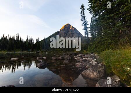 tall peak behind a lake with the sun rays hitting the top of the mountain Stock Photo