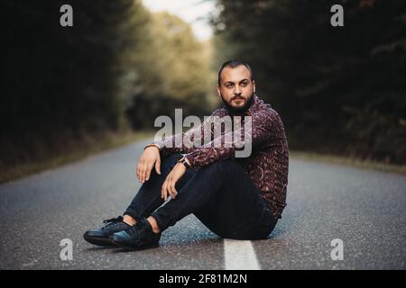 A handsome Caucasian male sitting on a road and posing Stock Photo