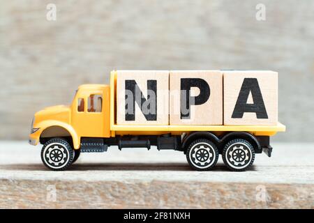 Toy truck hold alphabet letter block in word NPA (Abbreviation of Non performing assets or Nasopharyngeal airway) on wood background Stock Photo