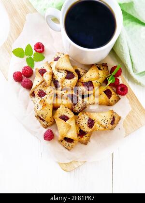 Cookies with raspberry jam, berries and mint on parchment on a plank, cup with coffee and napkin on wooden board background from above Stock Photo
