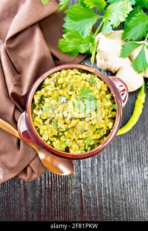Indian national dish kichari made of mung bean, rice, celery, spinach, hot pepper and spices in a bowl on a napkin, ginger and spoon on wooden board b Stock Photo