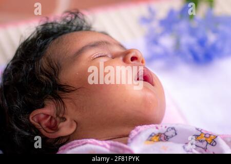 1-Month-old cute baby girl sleeping in a pink fluffy pillow, born with lots of black hair. Napping and dreaming time for the adorable infant. close up Stock Photo