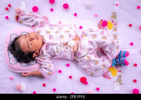 1-Month-old cute baby girls birthday celebration, sleeping in a pink fluffy pillow and matt, Napping and dreaming time for the infant. Overhead view o Stock Photo