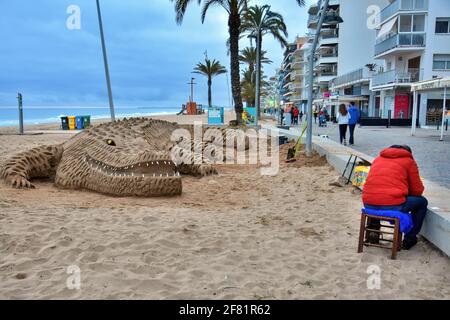 Calafell, Spain. 10th Apr, 2021. A street artist exhibits his work of a sand crocodile on the beach with very few people during the local confinement in Calafell. The Government of Catalonia once again orders the regional confinement due to the Covid-19 health crisis, reducing the mobility of people resulting to empty streets, beaches, restaurants, cafes and ice cream parlours being closed at 5:00 pm. (Photo by Ramon Costa/SOPA Images/Sipa USA) Credit: Sipa USA/Alamy Live News Stock Photo