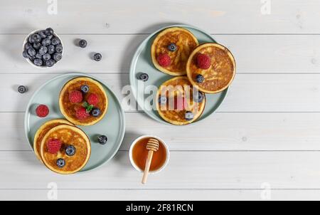 Two plates with tasty american pancakes with raspberries, blueberries, and honey. Breakfast concept with copy space. Stock Photo
