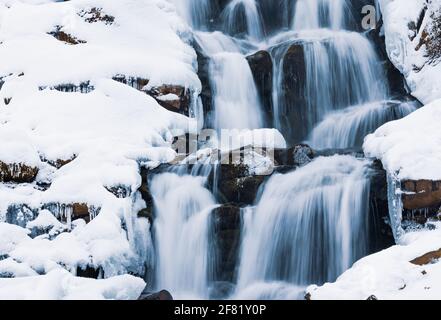 Small waterfall of cold water flow among the stones covered with snow Stock Photo