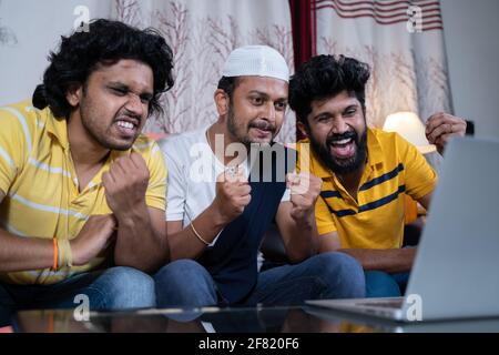 Diverse multi ethnic friends clapping and cheering up supporting team watching live streaming cricket sports match together on laptop - concept of Stock Photo