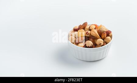Different types of nuts and dried fruits in a white cup on a light background with space to copy. Candied fruits and nut kernels. Stock Photo