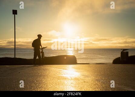Silhouette image of a cyclist getting ready to ride on the beach at sunrise