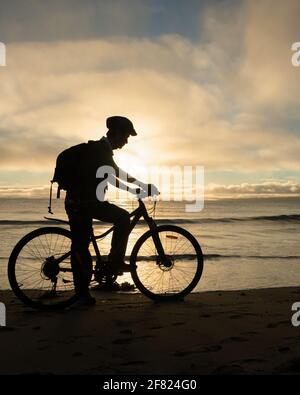 Silhouette image of a cyclist getting ready to ride on the beach at sunrise. Vertical format.