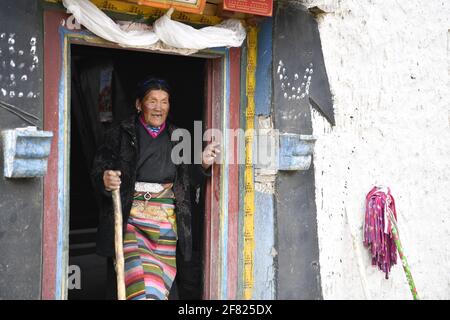 (210411) -- XIGAZE, April 11, 2021 (Xinhua) -- Lhapa stands at a door of her house in Puga Village of Xigaze, southwest China's Tibet Autonomous Region, March 20, 2021. Lhapa, born in 1945, is a villager in Puga Village. When she was a child, her mother became blind due to overwork and lost the ability to work. The serf owner drove her out of the manor, and Lhapa's mother had to beg everywhere with her sister for a living. In 1959, during the democratic reform in Tibet, the Lhapa's family were finally reunited and alloted 24 mu (about 1.6 hectare) of land, six sheep and two cows. They also Stock Photo