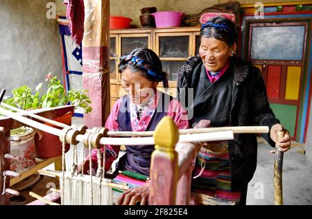 (210411) -- XIGAZE, April 11, 2021 (Xinhua) -- Lhapa (R) teaches her daughter weaving in Puga Village of Xigaze, southwest China's Tibet Autonomous Region, March 20, 2021. Lhapa, born in 1945, is a villager in Puga Village. When she was a child, her mother became blind due to overwork and lost the ability to work. The serf owner drove her out of the manor, and Lhapa's mother had to beg everywhere with her sister for a living. In 1959, during the democratic reform in Tibet, the Lhapa's family were finally reunited and alloted 24 mu (about 1.6 hectare) of land, six sheep and two cows. They al Stock Photo