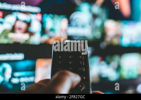 Video on demand screen with remote control in hand, entertainment Stock Photo