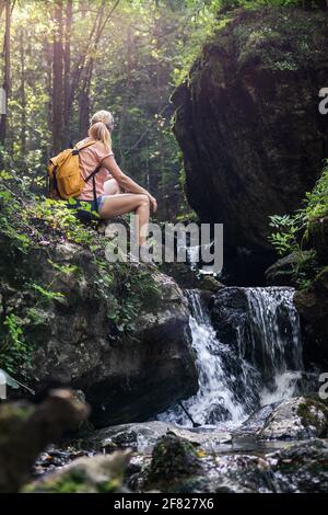 Woman resting during hike in wonderful nature. Hiker sitting on rock near a stream in forest at natural parkland Mala Fatra, Slovakia Stock Photo