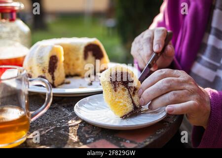 Serving slice of cake outdoors. Marbled bundt cake and tea on table. Refreshment in spring garden Stock Photo