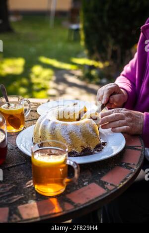 Serving slice of bundt cake outdoors. Easter cake and tea on table. Refreshment in spring garden Stock Photo