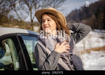 Young woman wearing cowboy hat and scarf. Traveler standing next to car during winter road trip Stock Photo