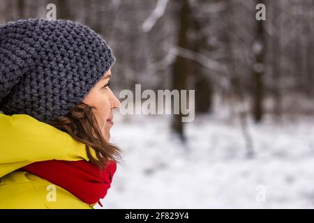 Woman with knit hat looking at snowy forest. Side view portrait of young woman wearing warm clothing in winter Stock Photo
