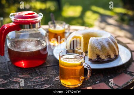 Tea in cup and teapot with bundt cake on table outdoors. Serving dessert and hot drink in spring garden. Picnic at springtime Stock Photo