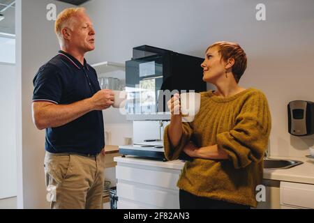 Man and woman having coffee break in office. Colleagues talking while having coffee in office. Stock Photo