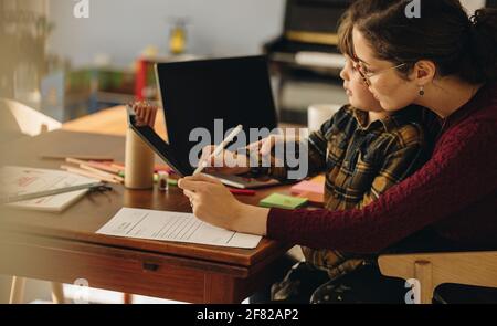 Mom teaching son on digital tablet. Boy learning to write on digital tablet with help from his mother at home. Stock Photo
